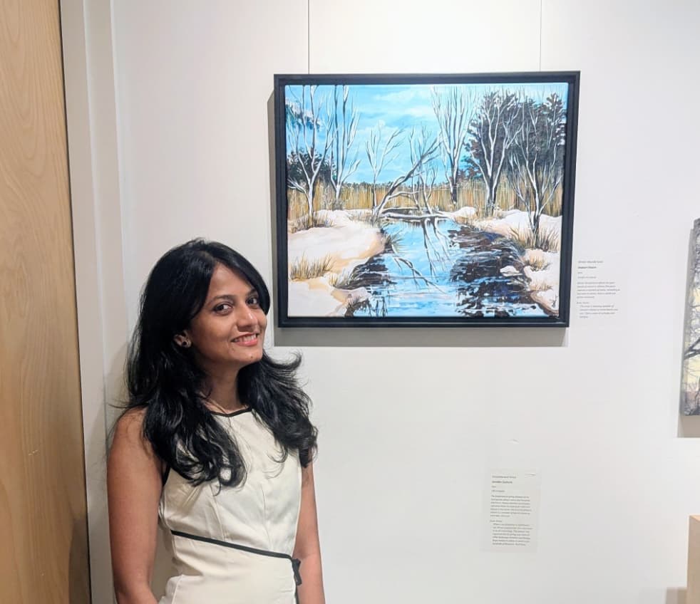Shabari Khaire standing beside one of her paintings at an exhibition